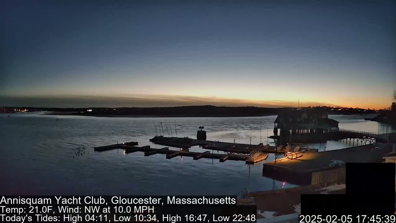 A twilight view of a marina with docked boats, a clubhouse, and a calm body of water under a clear, dark sky.