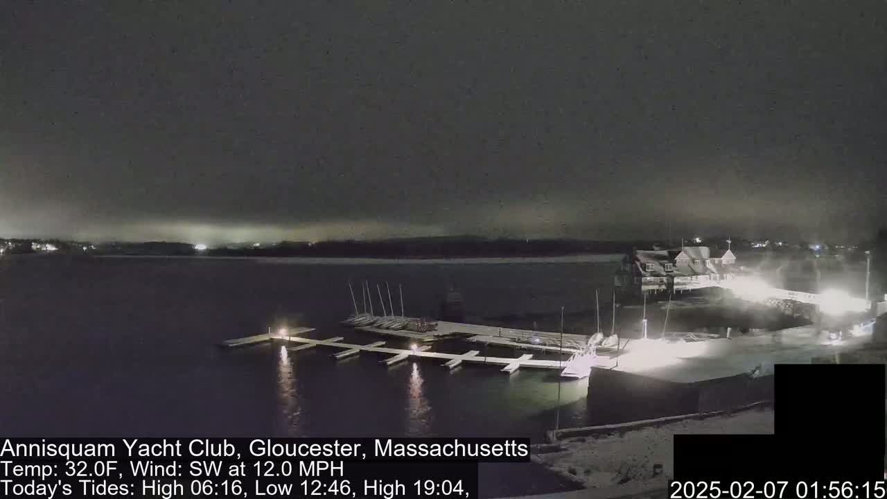 A snow-covered marina with docked sailboats is illuminated at night under a dark, overcast sky.