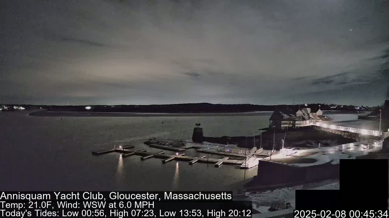 A nighttime view of a marina with a building and boats under a cloudy sky.