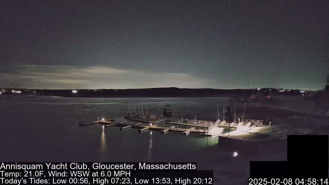 A nighttime view of a marina with boats docked, under a partly cloudy sky and a temperature of 21 degrees Fahrenheit.