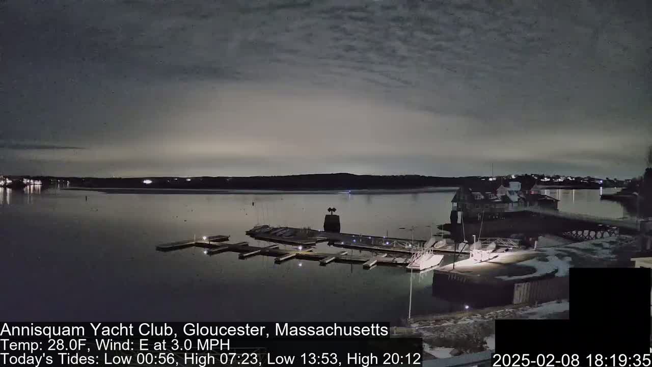 A nighttime view of a marina with boats docked, under a cloudy sky.