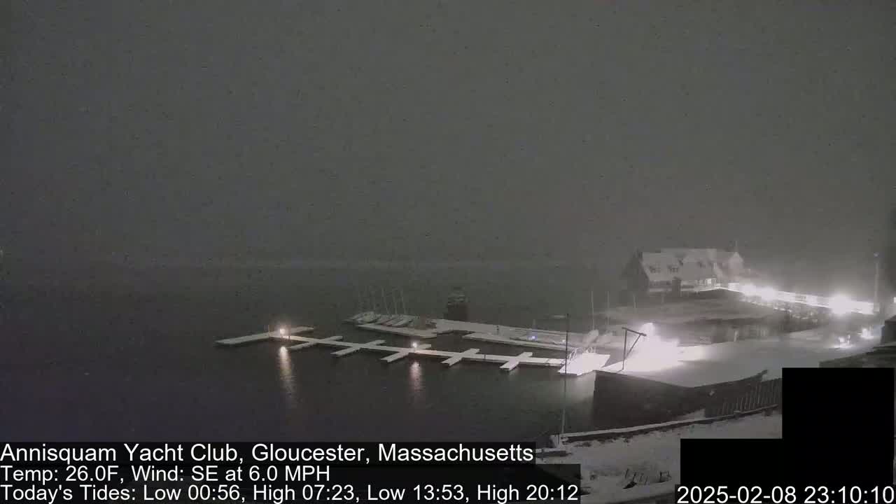 A snow-covered marina with docked boats is seen at night under a heavy snowfall.