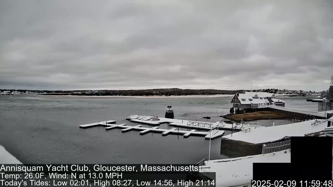 A snow-covered marina with a clubhouse sits on a calm bay under an overcast sky.