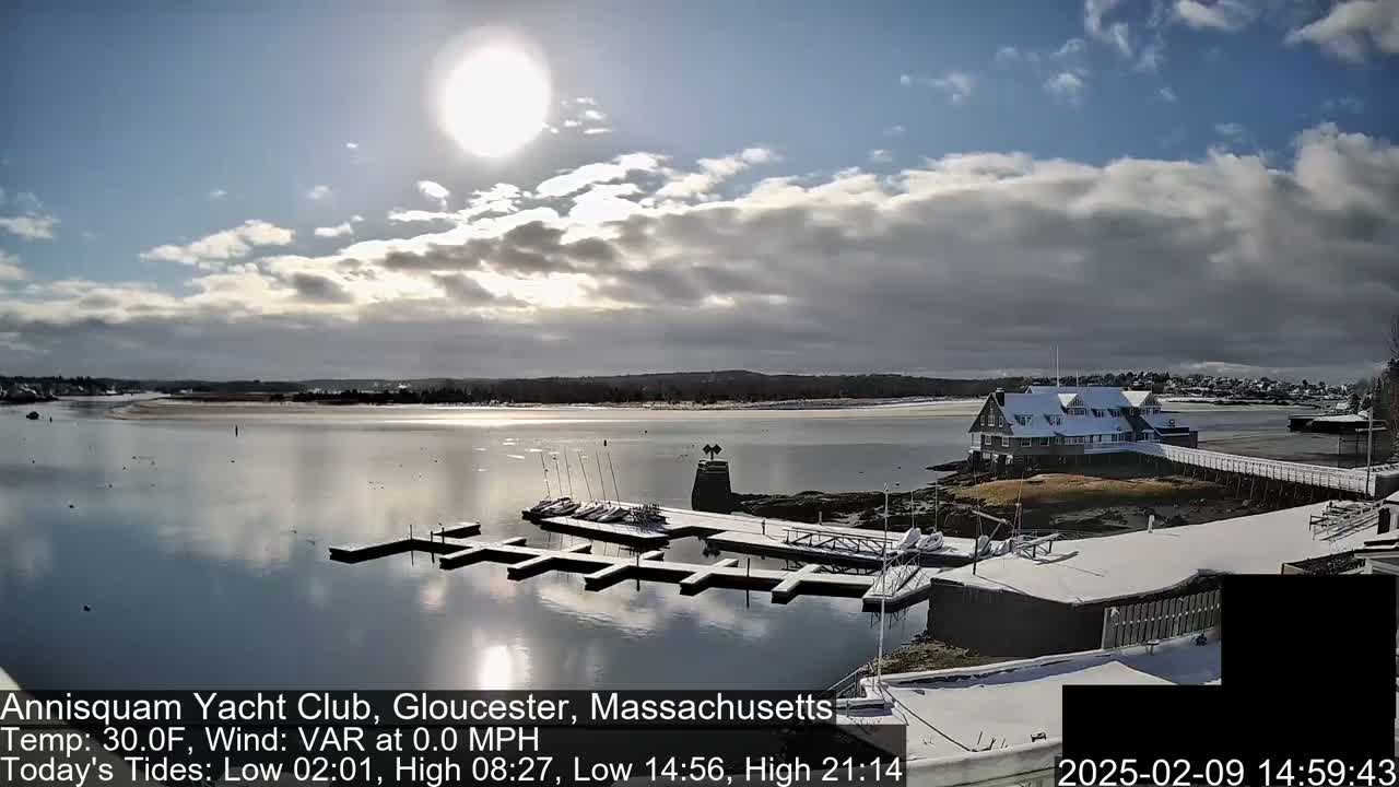 A snow-covered marina with a calm body of water under a partly sunny sky.