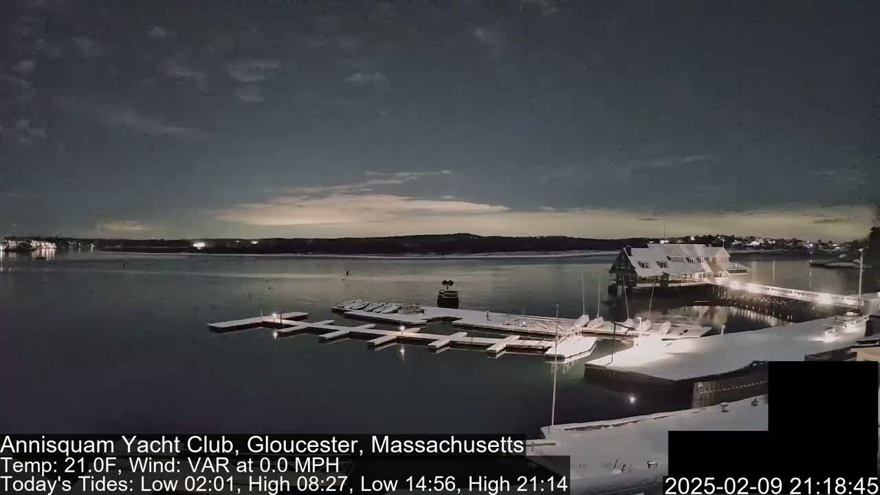 A snow-covered marina with boats docked at night under a partly cloudy sky.