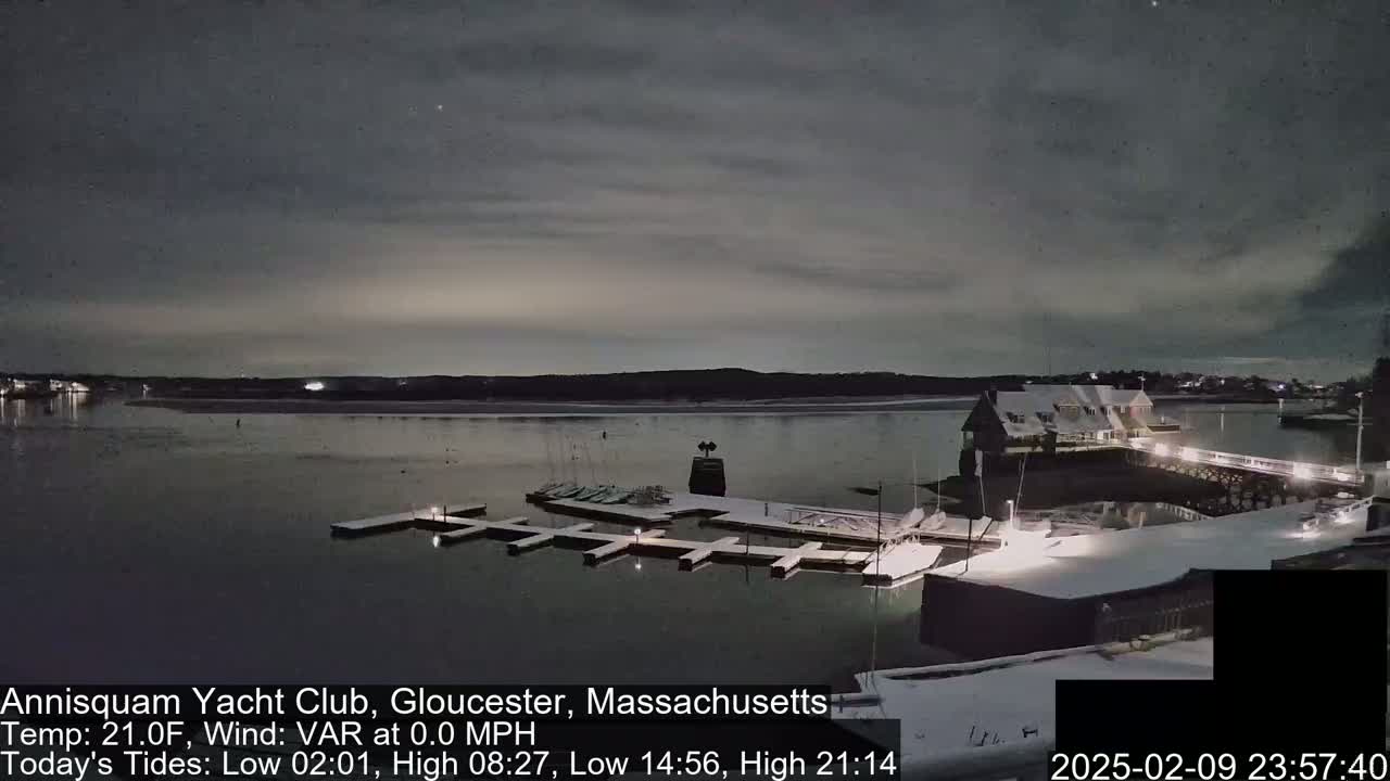 A snow-covered marina at night, under a mostly cloudy sky, sits on a calm body of water.