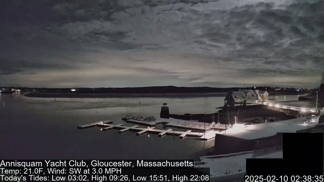 A snow-dusted marina with a calm body of water under a cloudy night sky.