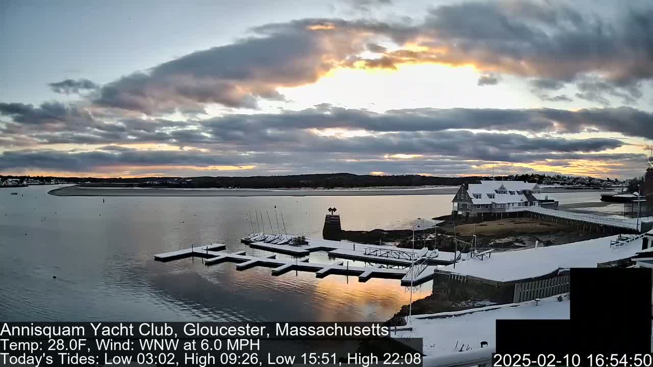 A snow-covered marina with boats at sunset under a partly cloudy sky.