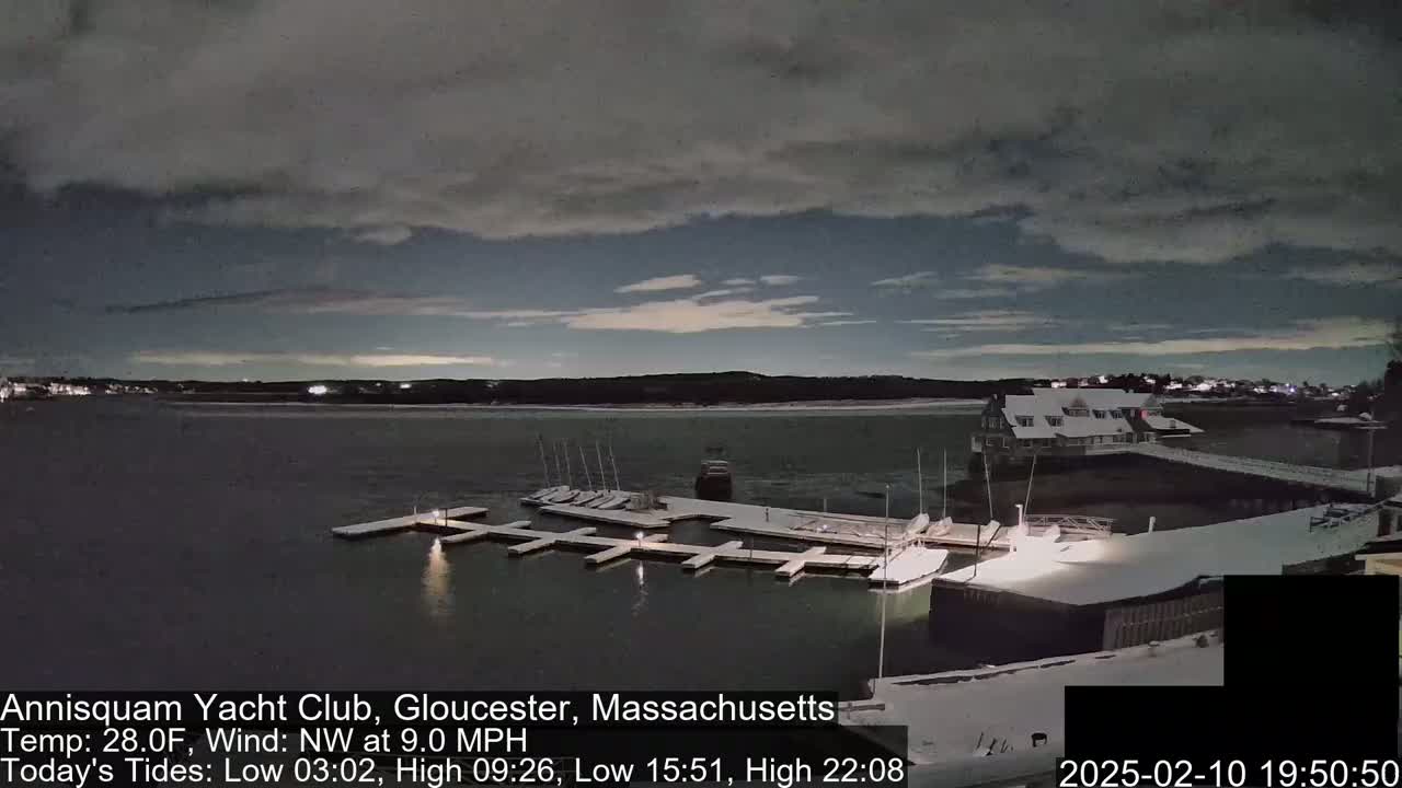 A snow-covered marina with numerous docked sailboats is visible under a dark, cloudy sky at night.