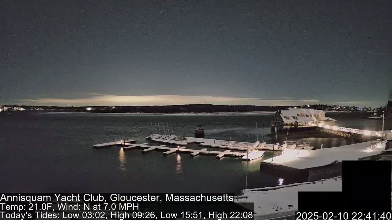 A snow-covered marina with docked sailboats is illuminated at night under a mostly clear, starry sky.