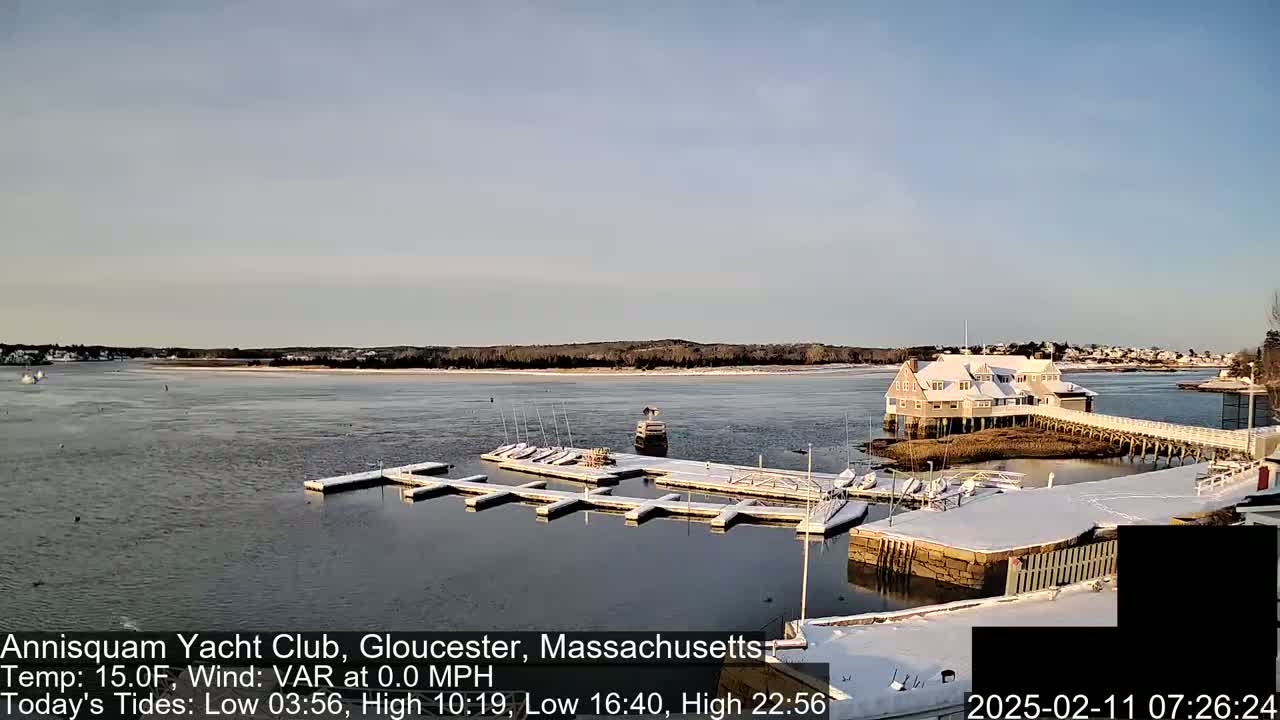 A snow-covered marina with boats docked, a building, and a calm body of water under a clear sky.
