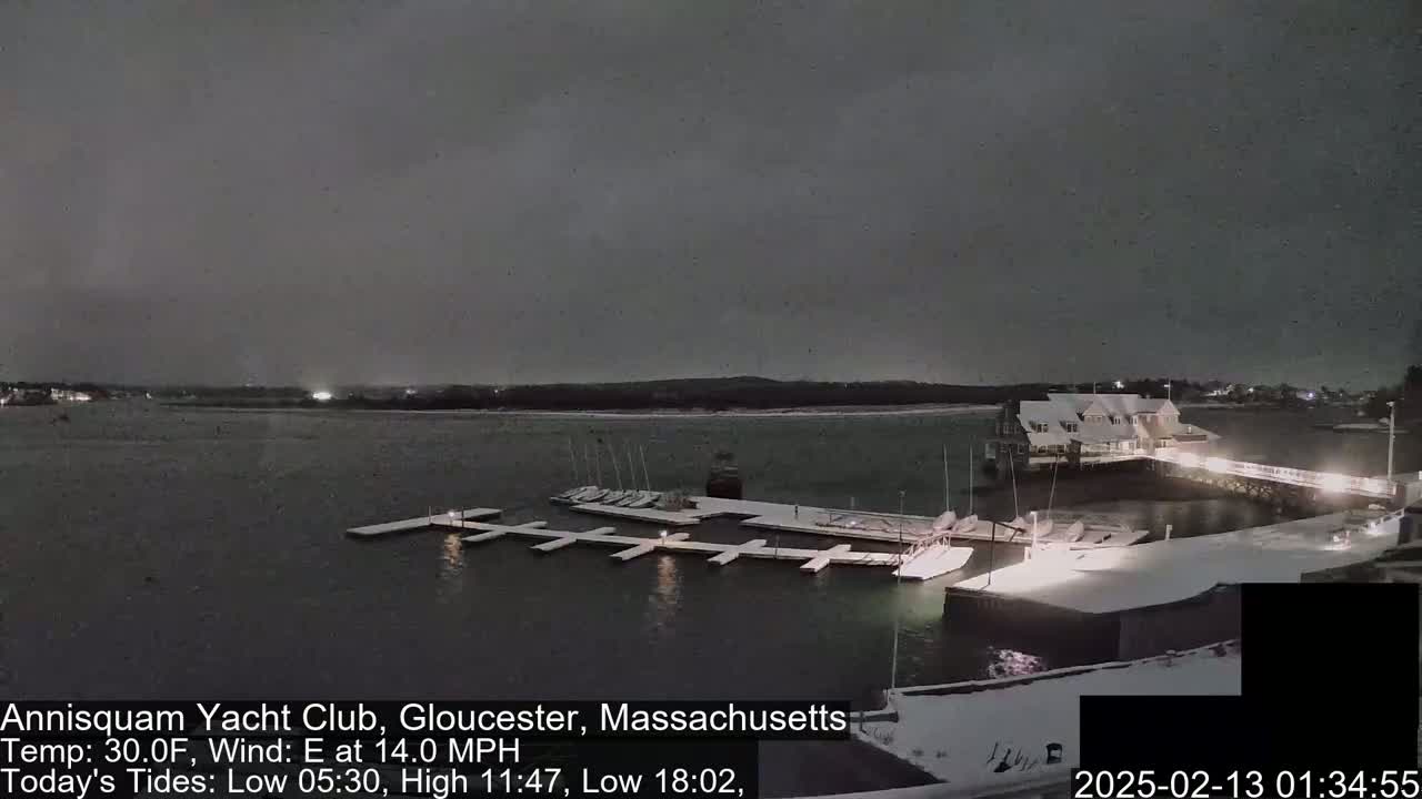 A snow-covered marina with boats docked at night under a dark, overcast sky.