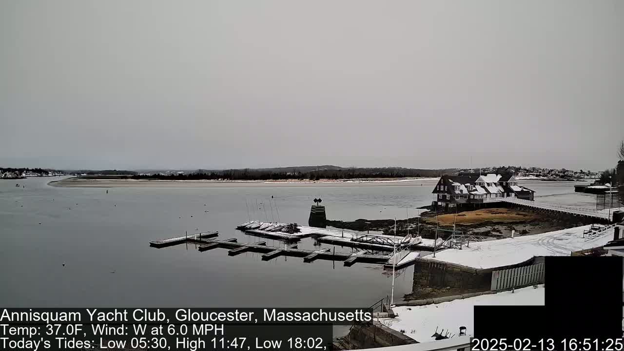 A snow-dusted marina with a clubhouse and several boats docked, under an overcast sky.