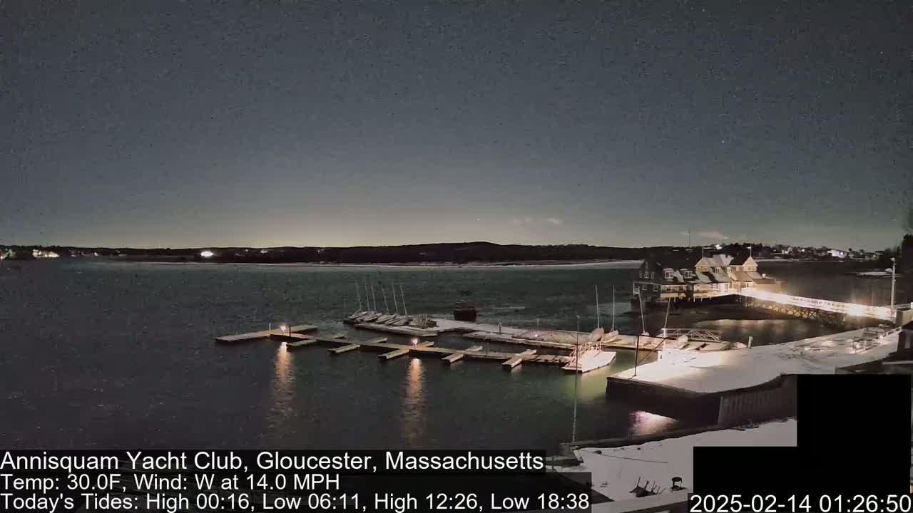 A nighttime view of a snow-dusted marina with sailboats docked under a dark, clear sky.