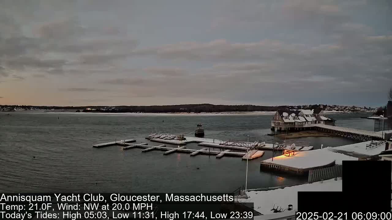A snow-covered marina with boats and a clubhouse is visible on a calm, overcast day.