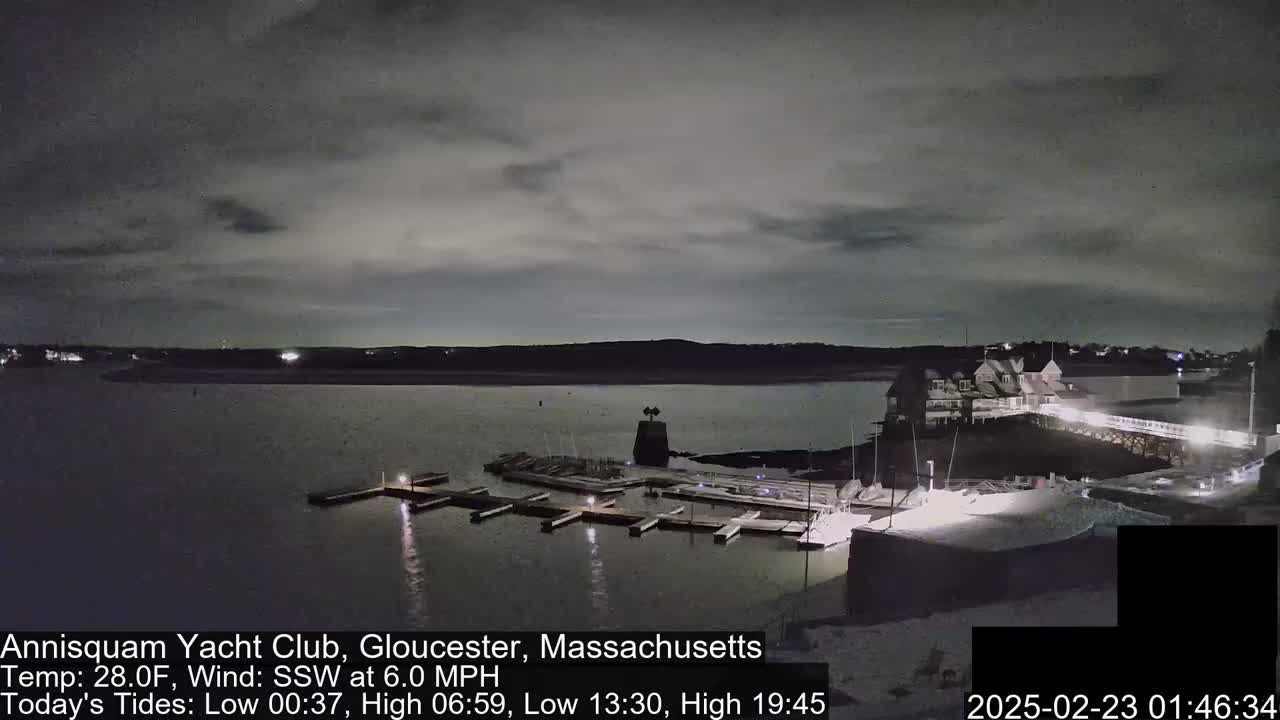A nighttime view of a marina with docked boats under a mostly cloudy sky.