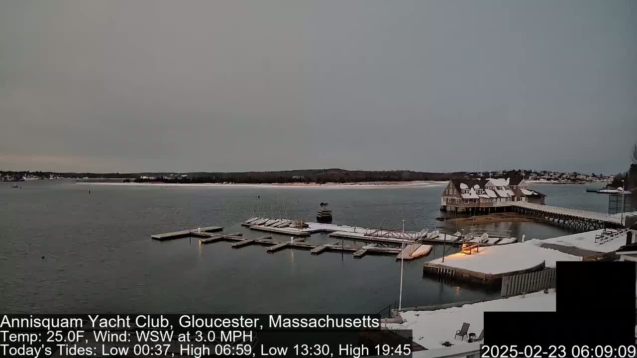 A snow-covered marina with boats docked, a clubhouse, and a pier under an overcast sky.