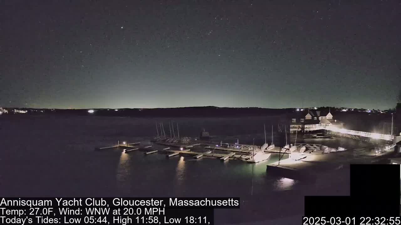 A nighttime, starlit view of a marina with sailboats docked, under a clear sky and a 20 mph wind.