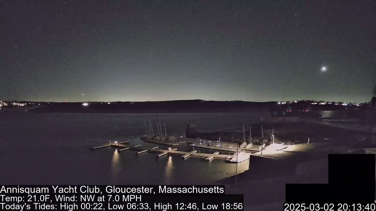 A nighttime view of a marina with docked boats under a partly cloudy sky and a visible moon.