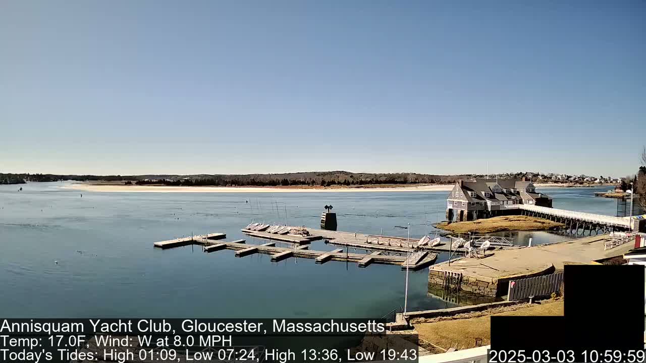 A marina with docked boats and a clubhouse is situated on a calm body of water under a clear blue sky.