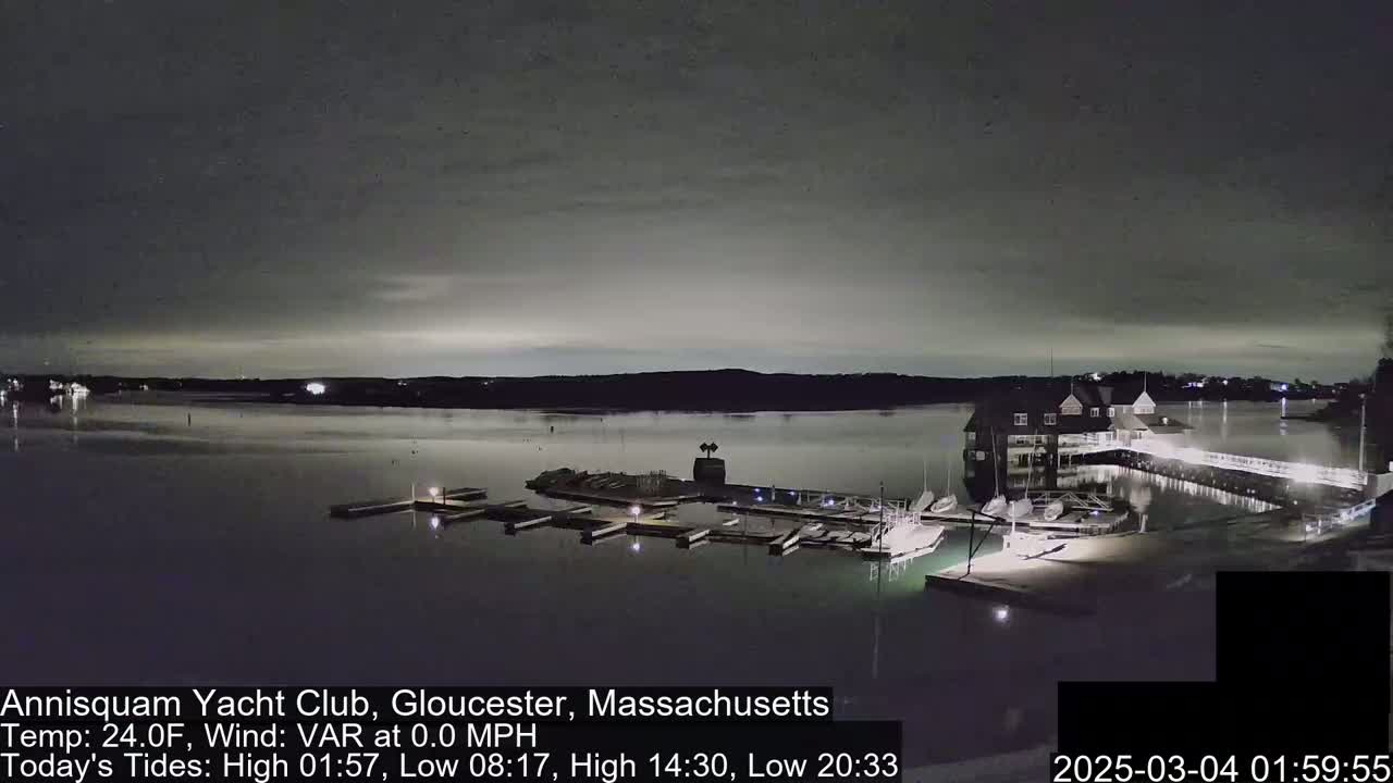A nighttime view of a marina with boats docked, under a mostly cloudy sky.