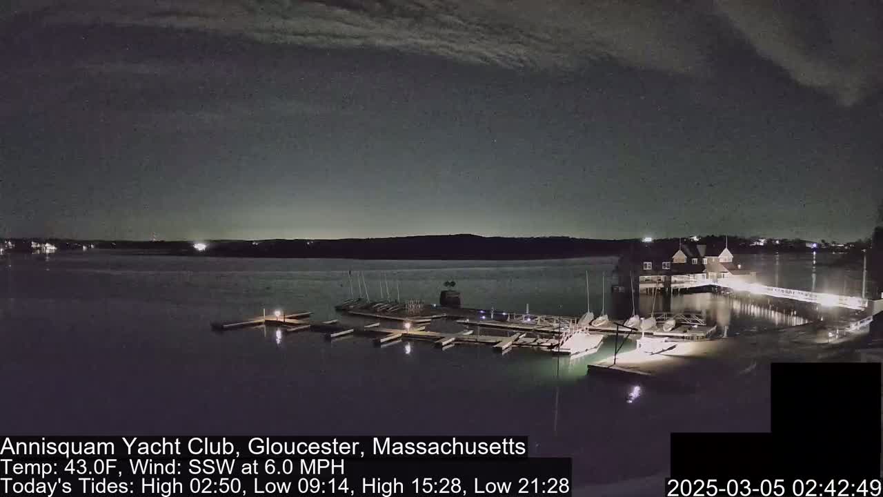 A nighttime view of a yacht club on a calm body of water under a partly cloudy sky.