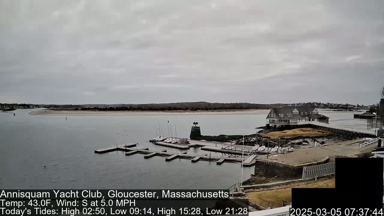 A yacht club sits on a rocky outcropping next to a calm body of water under an overcast sky.