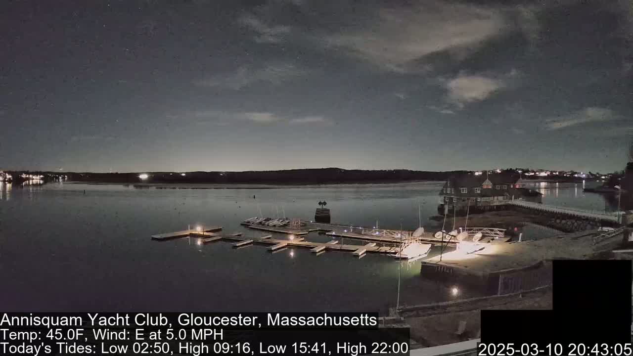 A nighttime view of a calm body of water with a marina and clubhouse under a partly cloudy sky.