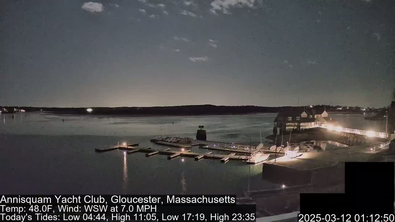 A nighttime view of a marina with docked boats and a clubhouse, under a partly cloudy sky.