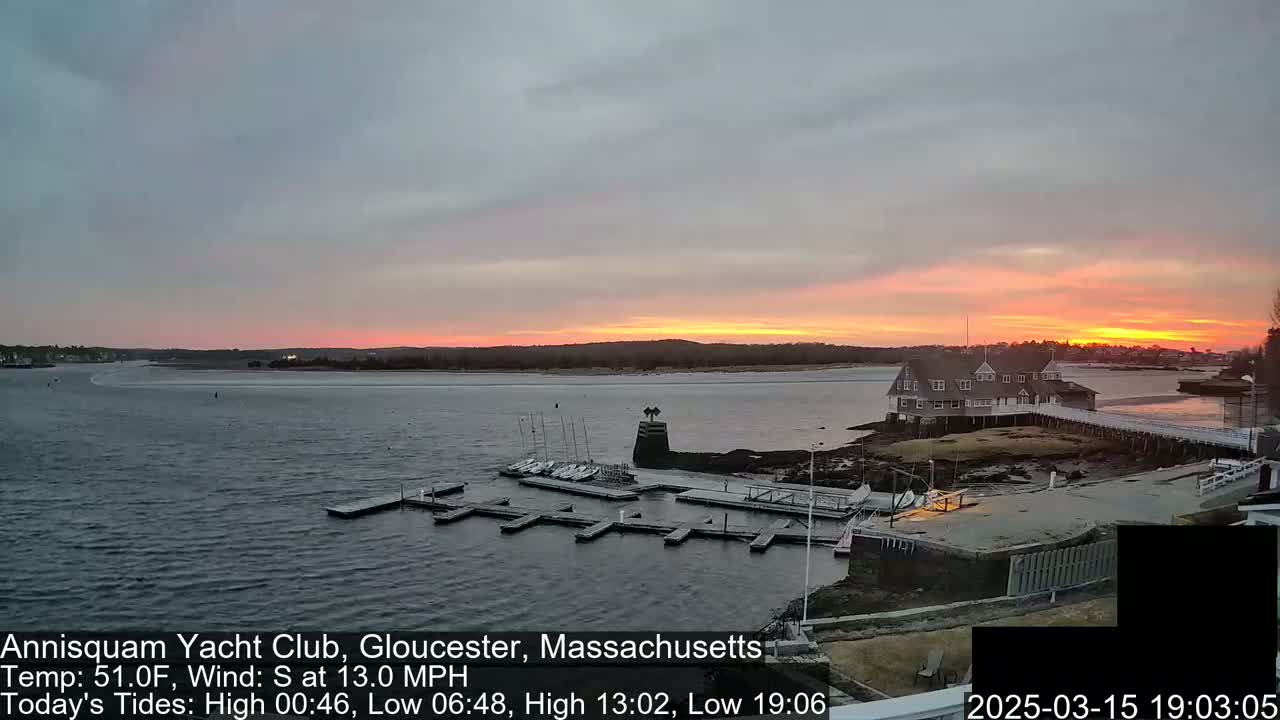 A calm bay at sunset, with a yacht club and several small boats docked, under a mostly clear sky with a pink and orange horizon.