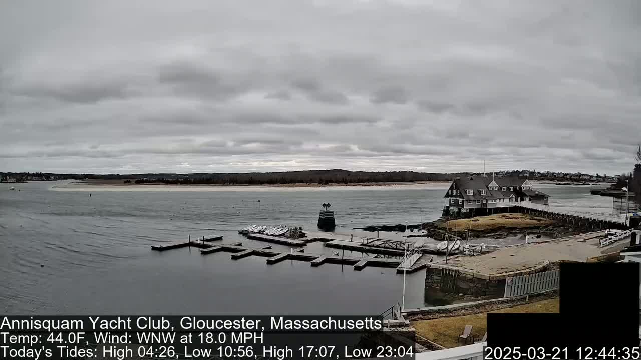 A calm body of water with docked boats and a clubhouse under an overcast sky.