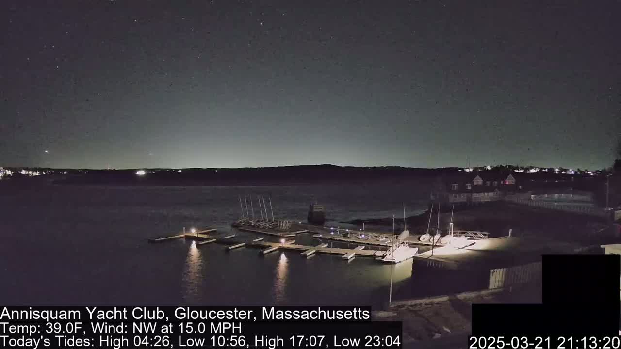 A nighttime view of a marina with boats docked under a partly cloudy sky and a 15 mph northwest wind.