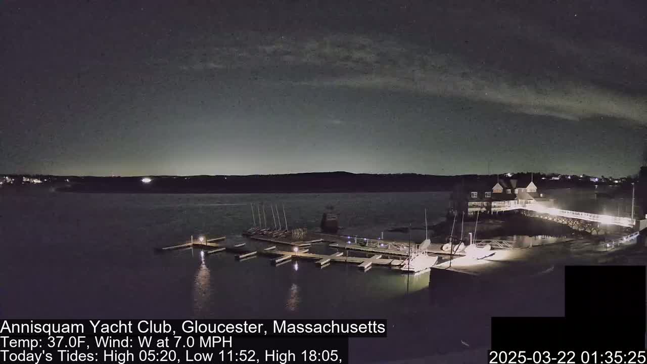 A nighttime view of a yacht club marina with boats docked under a partly cloudy sky and a 7 mph westerly wind.