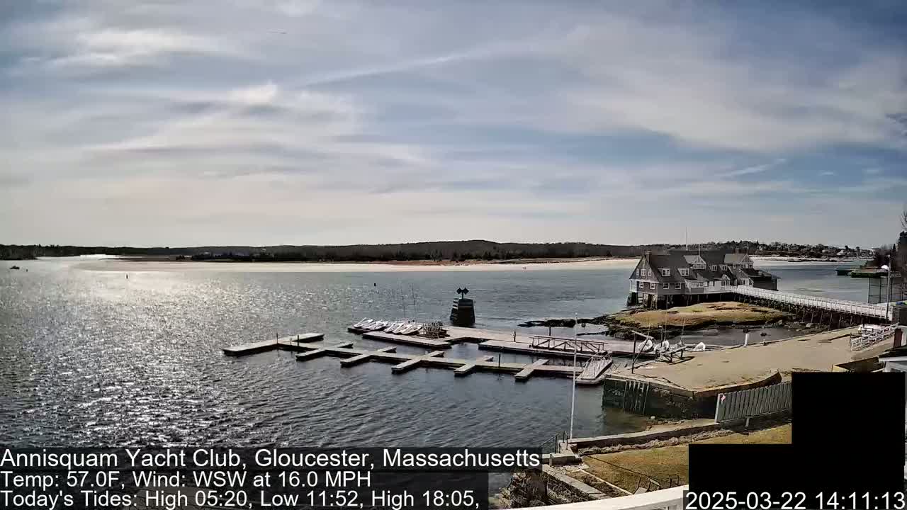 A marina with docked boats and a clubhouse is situated on a calm body of water under a partly cloudy sky.