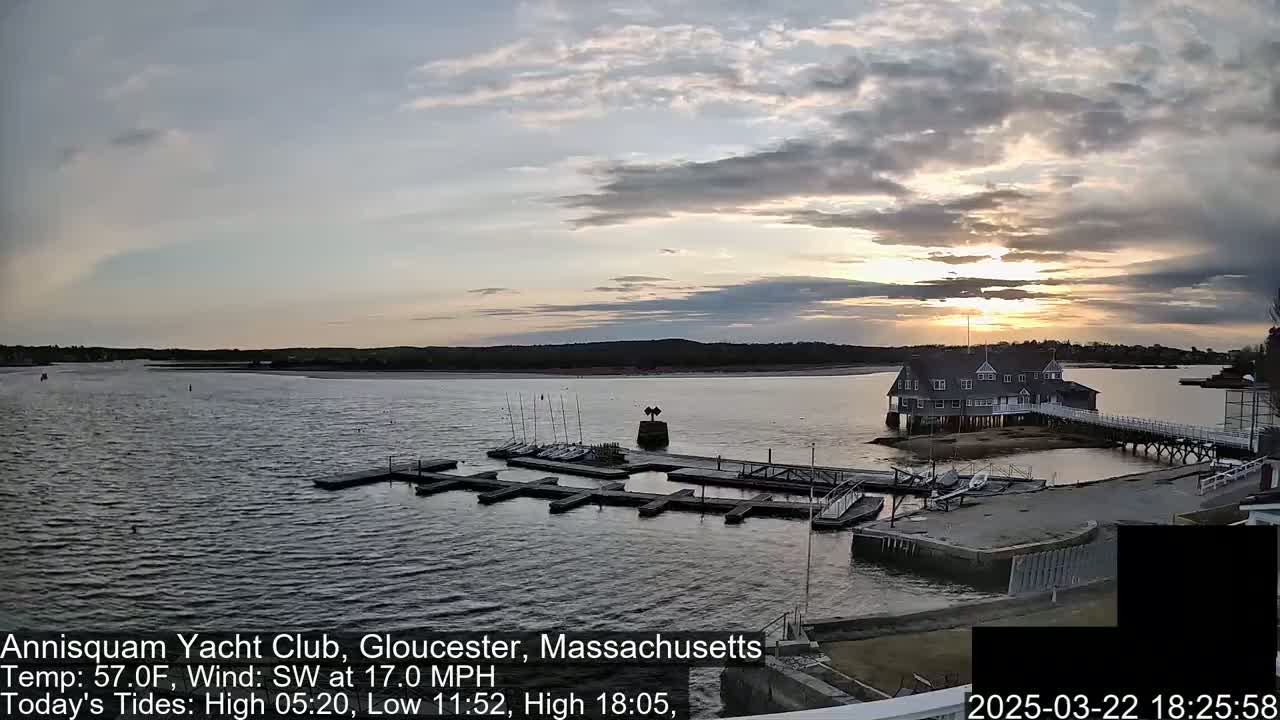 A calm body of water at sunset, showing a yacht club with docked sailboats under a partly cloudy sky.