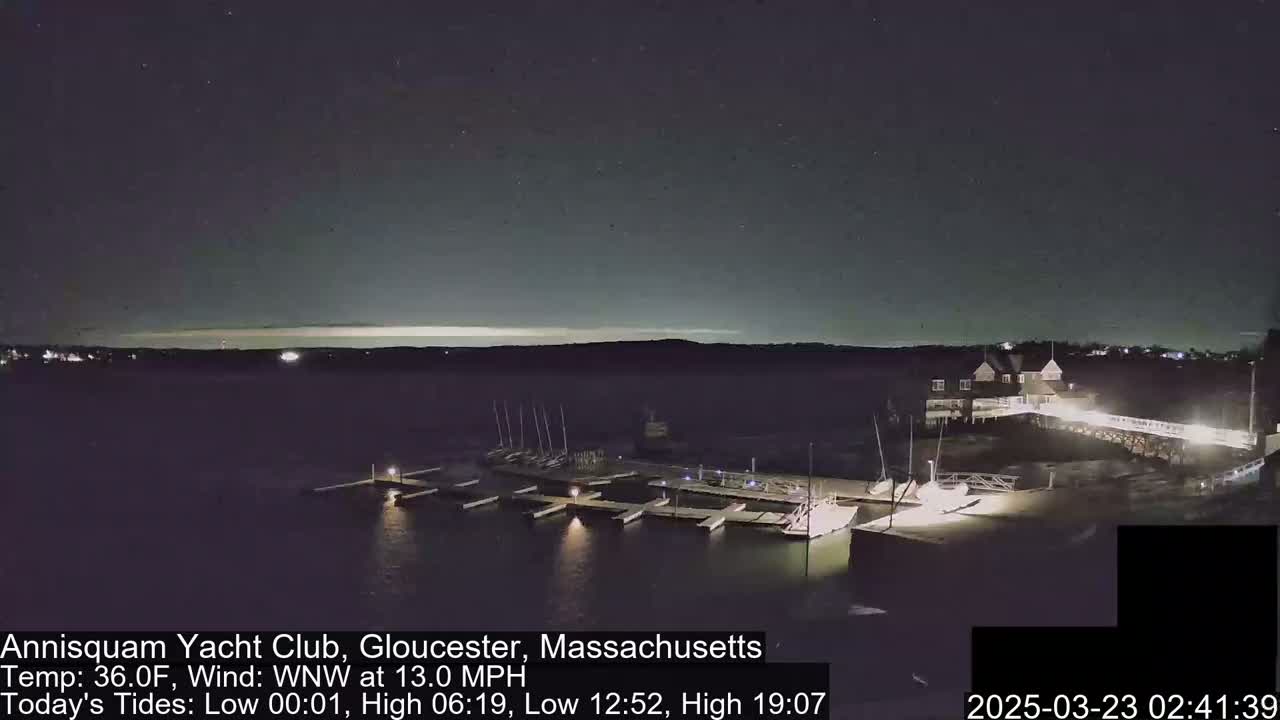 A nighttime view of a marina with boats docked, under a mostly clear sky, with a 36°F temperature and a 13 mph wind from the west-northwest.