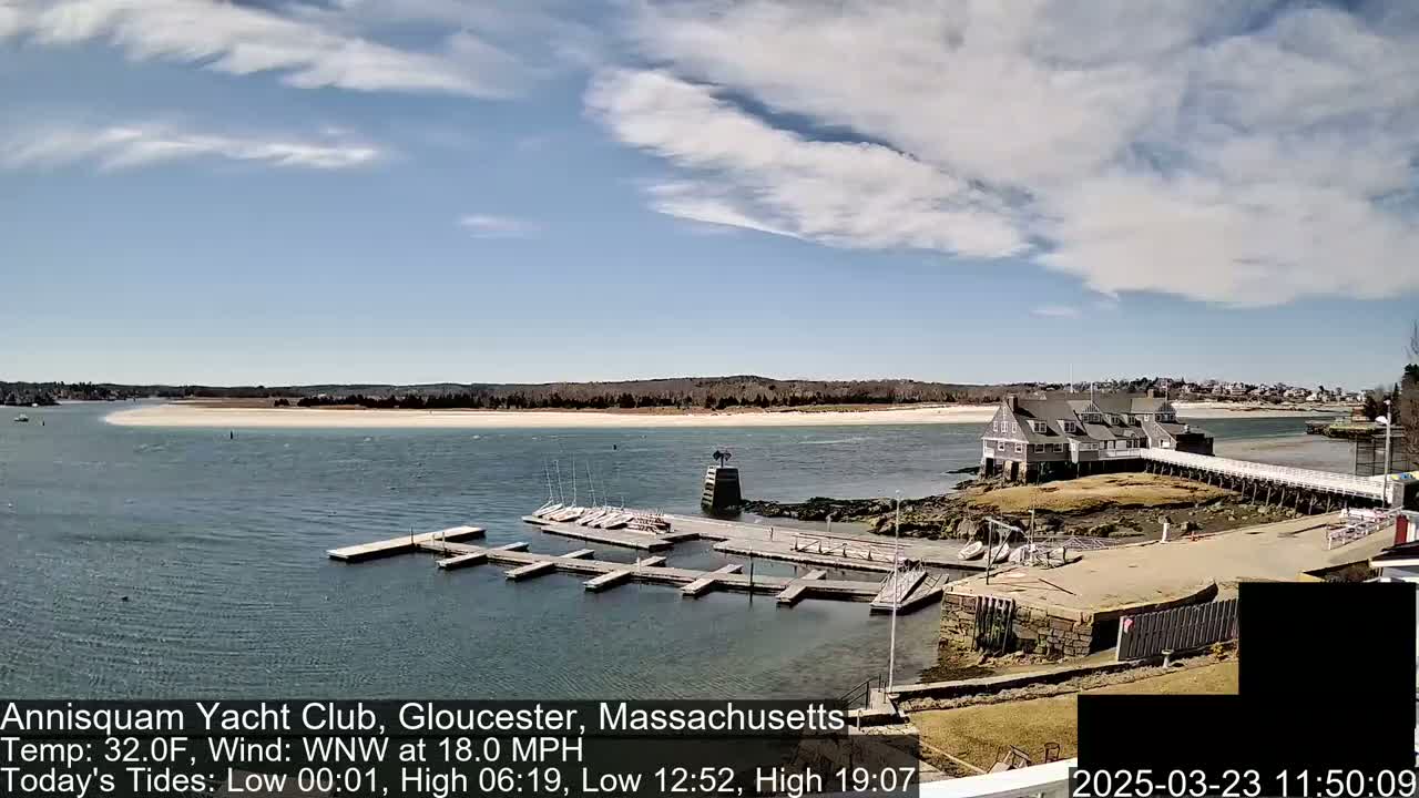A yacht club on a rocky shoreline with a sandy beach in the background under a partly cloudy sky.