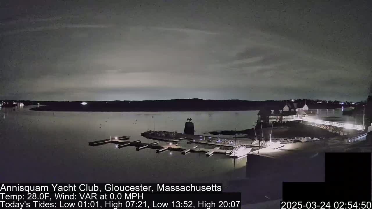 A nighttime view of a calm body of water with a marina and a building, under a cloudy sky.