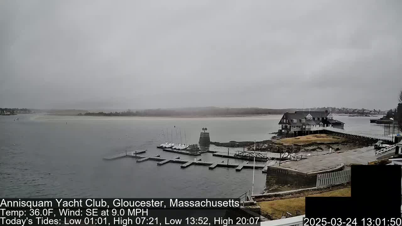 A yacht club sits on a rocky shoreline overlooking a calm body of water under an overcast sky.