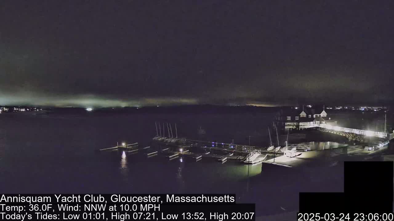 A nighttime view of a marina with boats docked, under a dark, cloudy sky.
