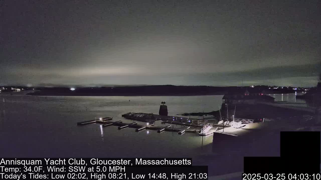 A nighttime view of a marina with boats docked, under a dark, cloudy sky.