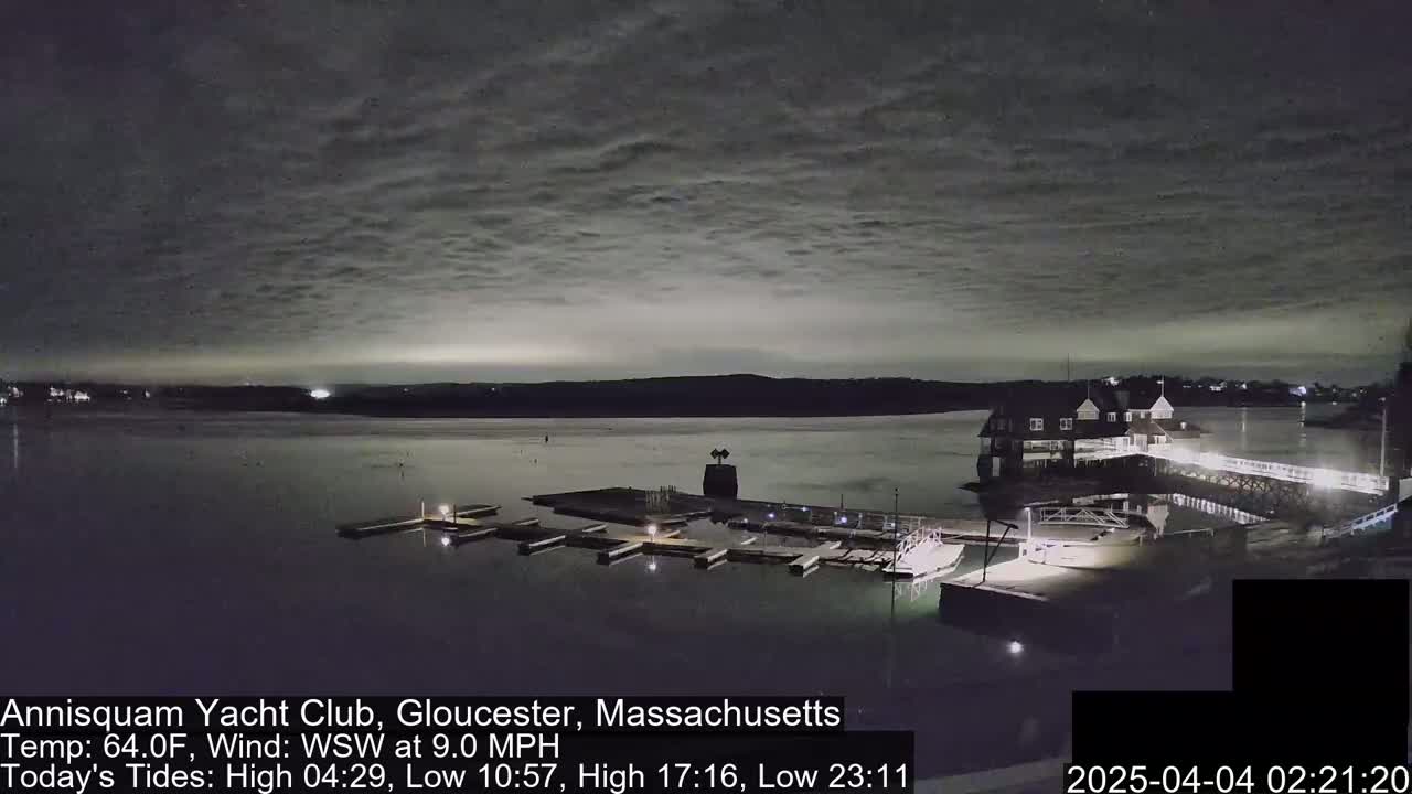 A nighttime view of a calm body of water with a marina, a clubhouse, and a partly cloudy sky.