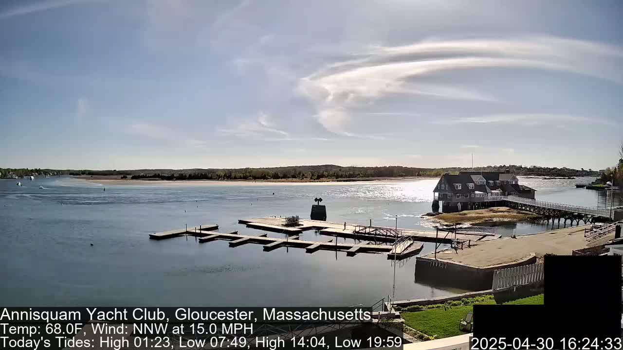 A marina with a clubhouse sits on a calm body of water under a partly cloudy sky.