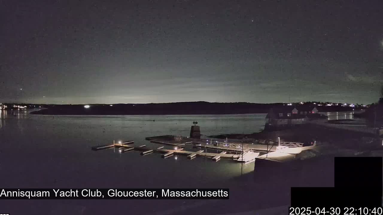 A nighttime view of a calm body of water with docks and a building on the shore under a mostly clear, dark sky.