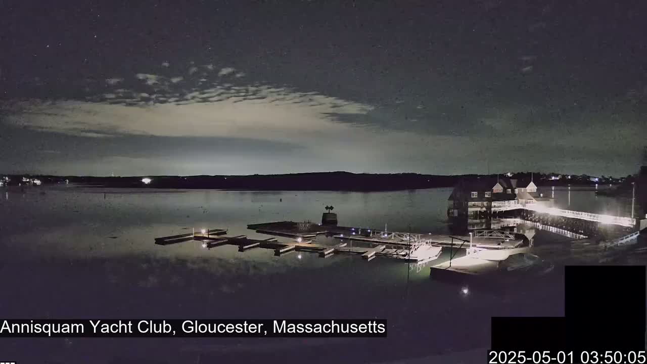 A nighttime view of a calm body of water with a marina and clubhouse under a partly cloudy sky.