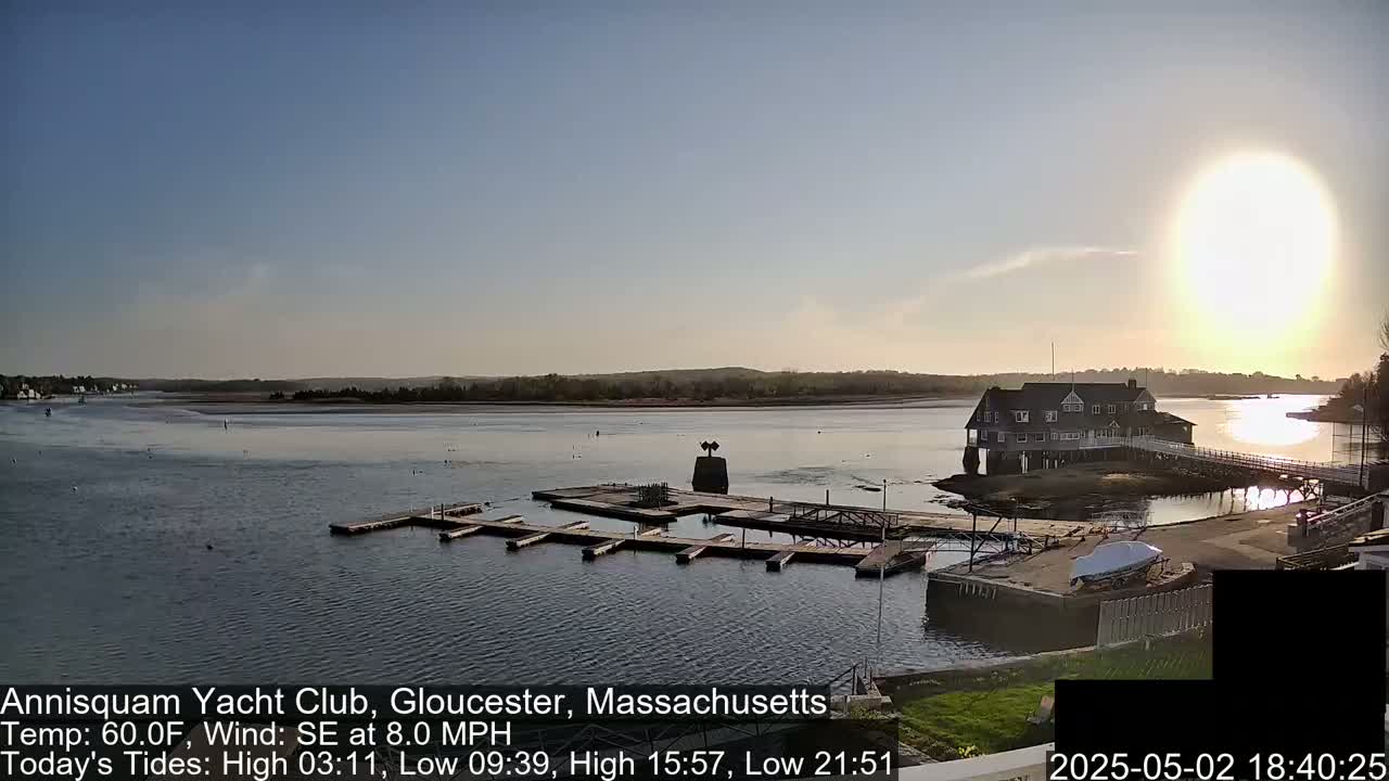A calm bay with a marina and clubhouse, under a partly cloudy sky with a bright sun.
