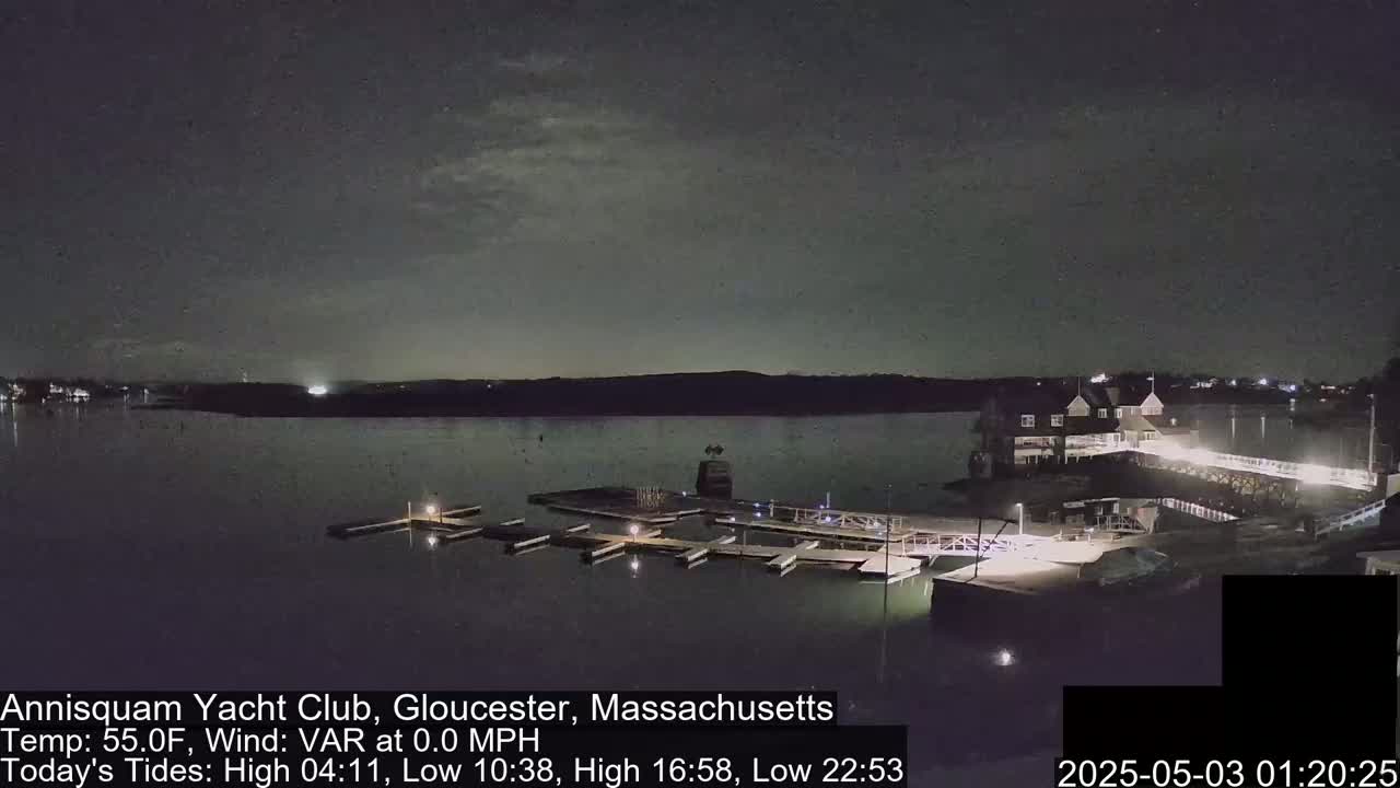 A nighttime view of a calm body of water with a marina and a clubhouse under a partly cloudy sky.