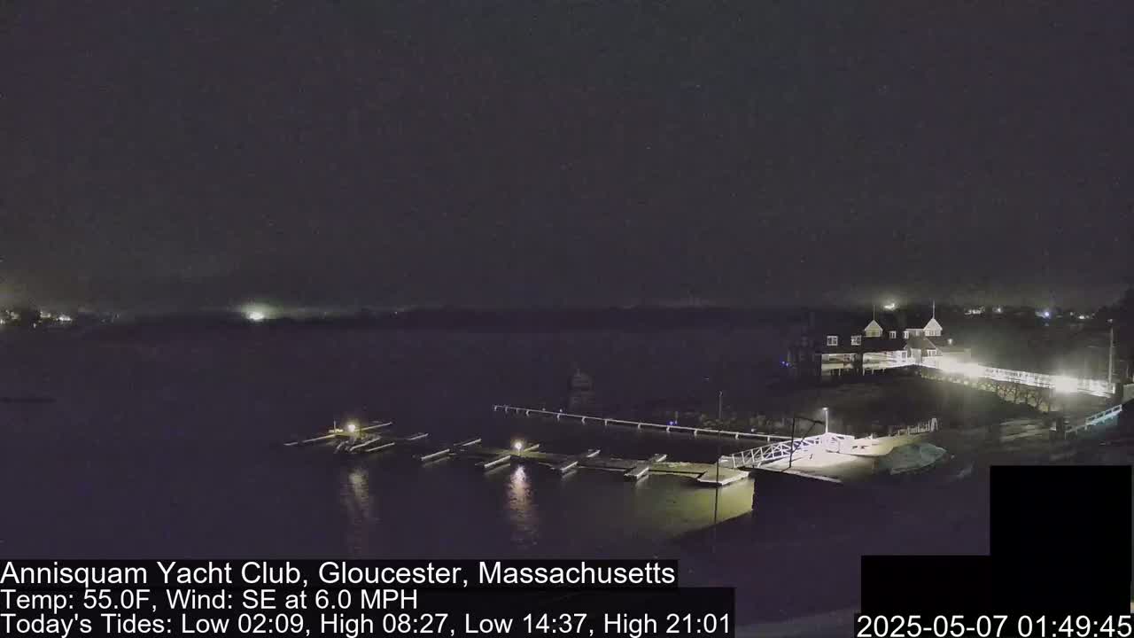 A nighttime view of a marina with boats docked, a clubhouse, and a walkway under a clear, dark sky.