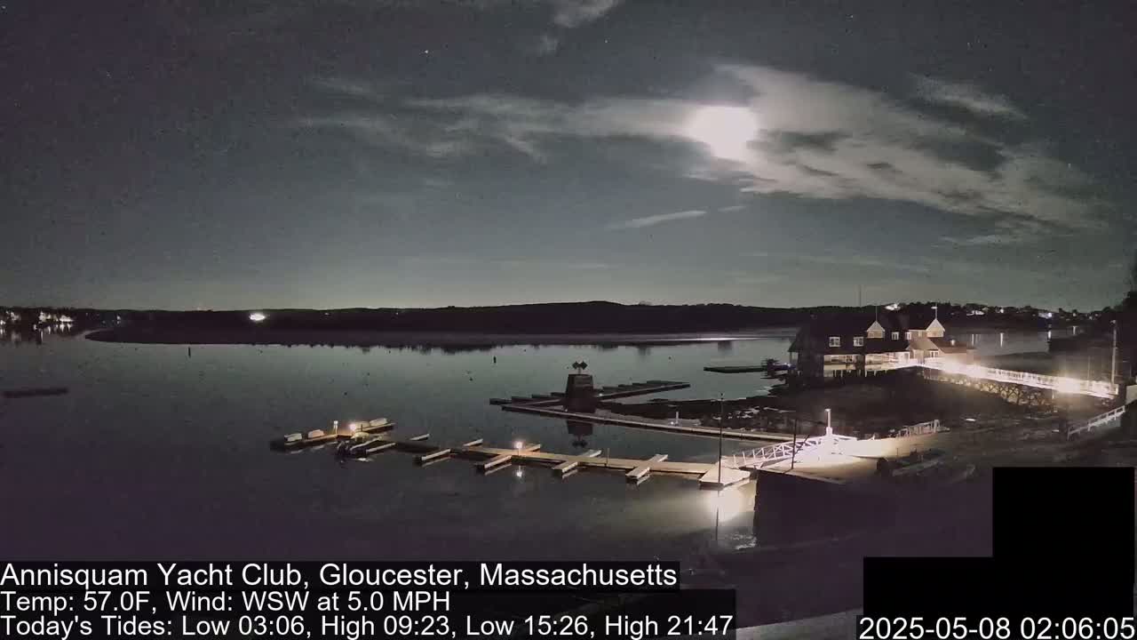 A moonlit night scene shows a calm body of water with docks and a clubhouse, under a partly cloudy sky.