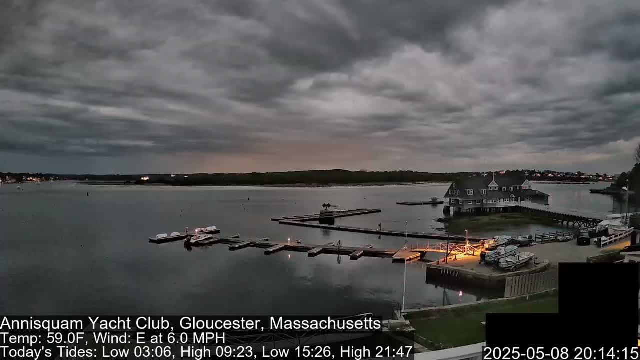 A marina with several boats docked under a mostly cloudy, dusky sky.